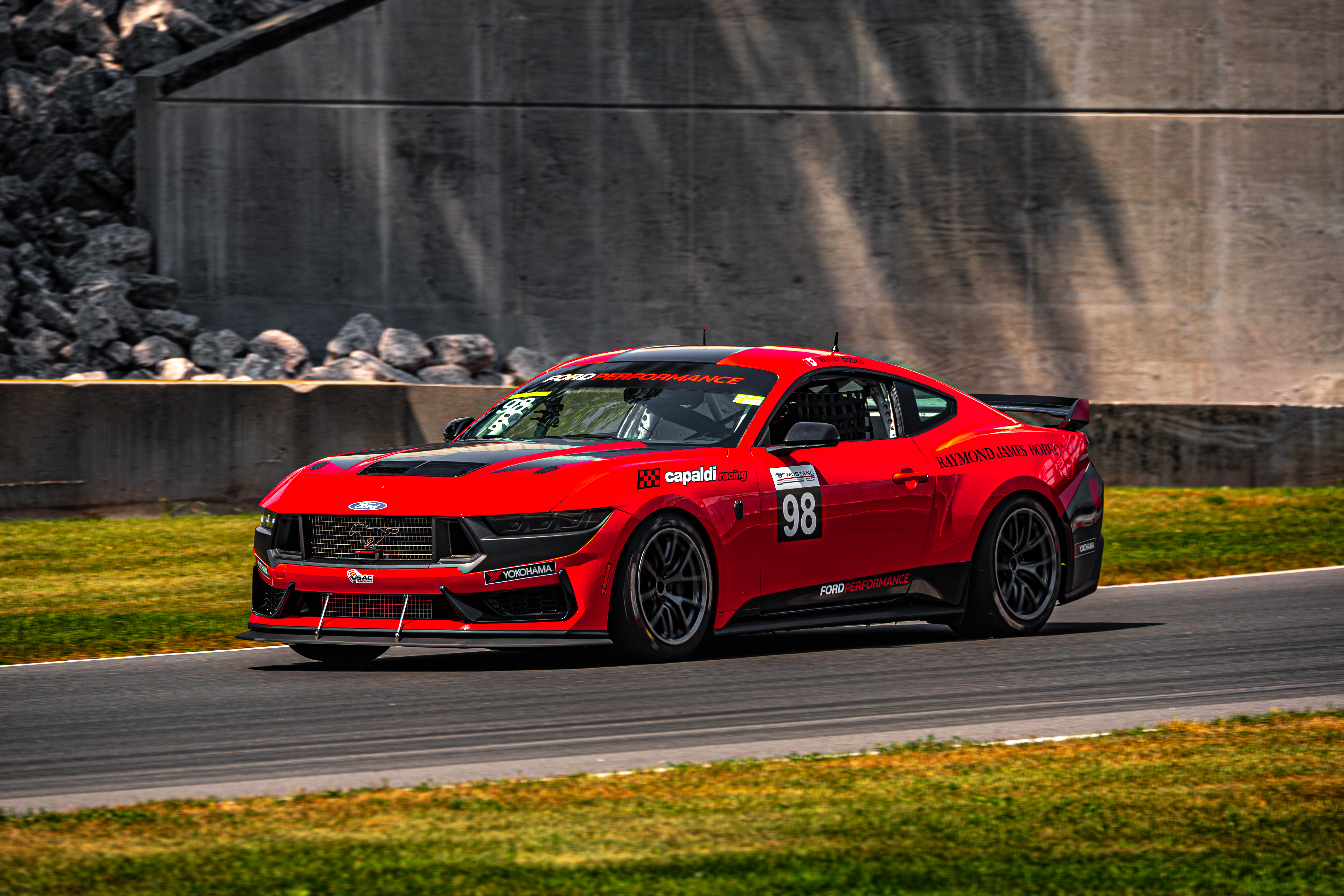 A red Mustang races around a track.